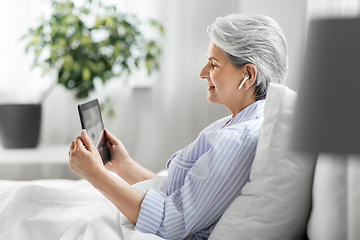 Image showing senior woman with tablet pc and earphones in bed