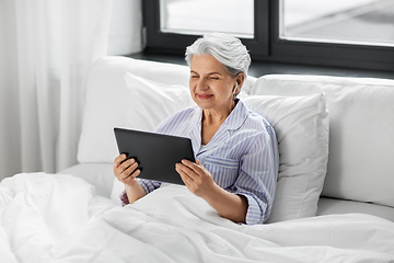 Image showing senior woman with tablet pc and earphones in bed