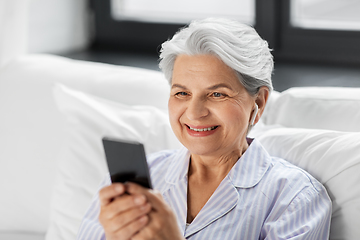 Image showing senior woman with smartphone and earphones in bed