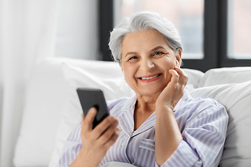 Image showing senior woman with smartphone and earphones in bed