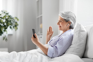 Image showing senior woman with phone having video call in bed