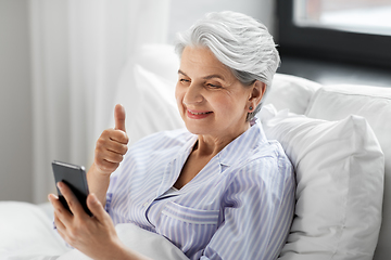 Image showing senior woman with phone having video call in bed