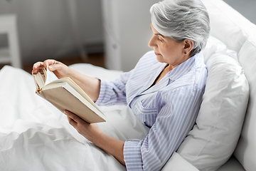 Image showing senior woman reading book in bed at home bedroom