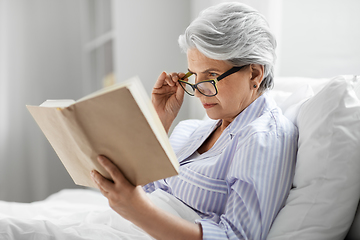 Image showing old woman in glasses reading book in bed at home