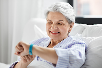 Image showing happy old woman with health tracker sitting in bed