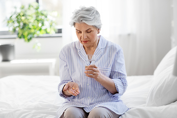 Image showing senior woman with pill and water sitting on bed