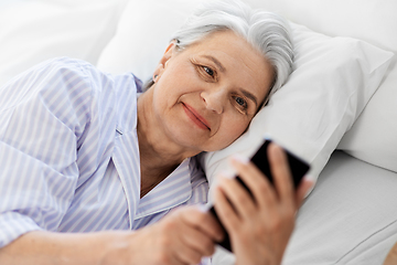 Image showing happy senior woman with smartphone in bed at home