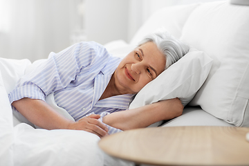 Image showing happy senior woman lying in bed at home bedroom
