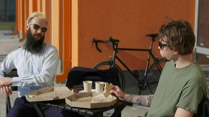 Image showing Friendly talk. Two happy young men eating pizza and talking to each other while sitting outdoors.