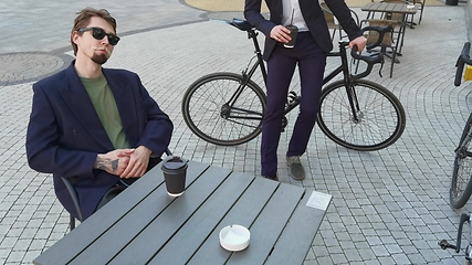 Image showing Two young men friends dressed casually spending time together at the city, drinking takeaway coffee next bike.