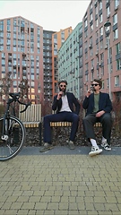 Image showing Two young men friends dressed casually spending time together at the city, drinking takeaway coffee next bike.