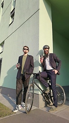 Image showing Two young men friends dressed casually spending time together at the city, drinking takeaway coffee next bike.