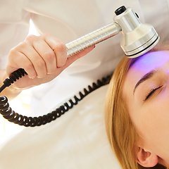 Image showing Young healthy woman with good skin doing cosmetic procedures in spa clinic. Light treatment.