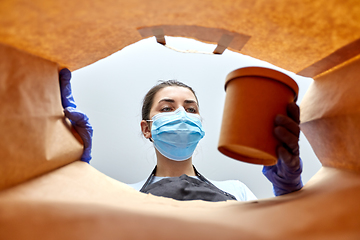 Image showing saleswoman in gloves and mask packing food in bag