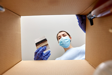 Image showing woman in mask unpacking parcel box with hair bands