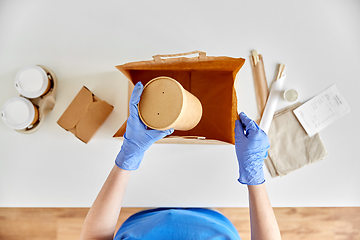 Image showing delivery woman in gloves packing food and drinks