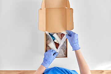 Image showing hands in gloves packing parcel box with cosmetics