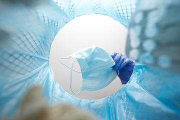 Image showing hand throwing used medical mask into trash can