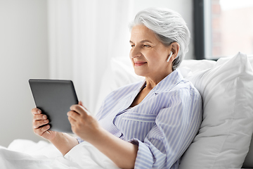 Image showing senior woman with tablet pc and earphones in bed