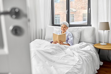 Image showing senior woman reading book in bed at home bedroom