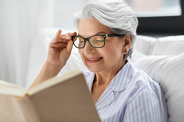 Image showing old woman in glasses reading book in bed at home