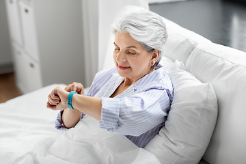 Image showing happy old woman with health tracker sitting in bed