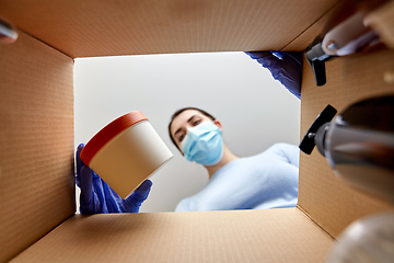 Image showing woman in mask unpacking parcel box with cosmetics