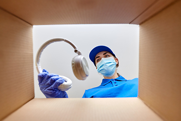 Image showing woman in mask packing headphones into parcel box