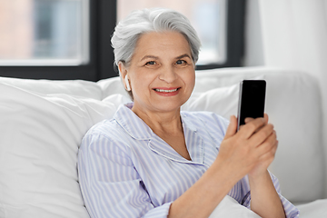 Image showing senior woman with smartphone and earphones in bed