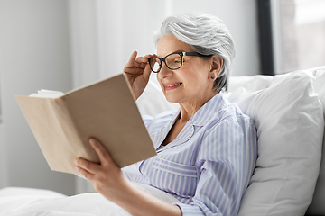 Image showing old woman in glasses reading book in bed at home