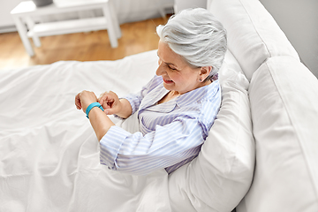 Image showing happy old woman with health tracker sitting in bed