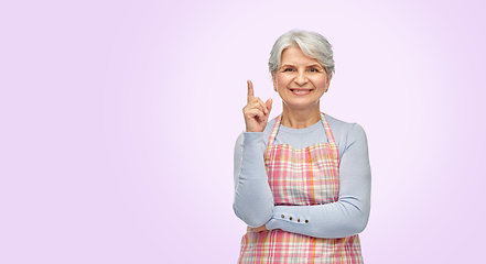 Image showing smiling senior woman in apron pointing finger up