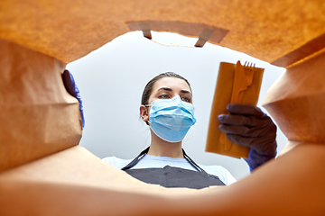 Image showing saleswoman in gloves and mask packing food in bag