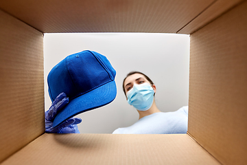 Image showing woman in mask opening parcel box with clothes