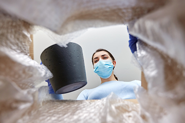 Image showing woman in mask opening parcel box with flower pot