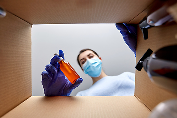 Image showing woman in mask unpacking parcel box with cosmetics