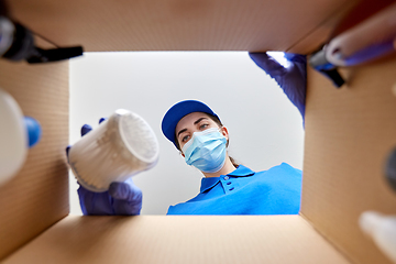 Image showing woman in mask unpacking parcel box with cosmetics