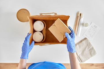 Image showing delivery woman in gloves packing food and drinks