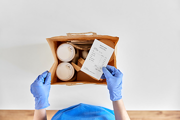 Image showing delivery woman in gloves packing food and drinks