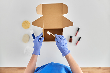 Image showing hands in gloves packing parcel box with cosmetics