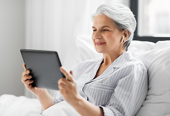 Image showing senior woman with tablet pc and earphones in bed