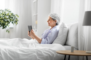 Image showing senior woman with tablet pc and earphones in bed