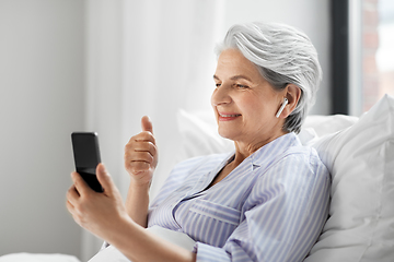 Image showing senior woman with phone having video call in bed