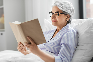 Image showing old woman in glasses reading book in bed at home