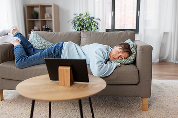 Image showing bored man with tablet pc lying on sofa at home