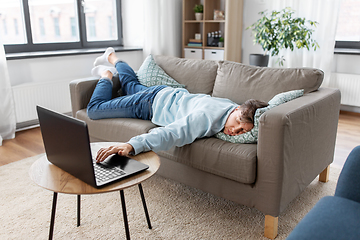 Image showing bored man with laptop lying on sofa at home