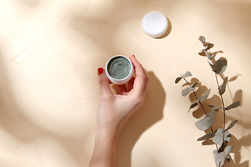 Image showing hand holding jar of blue cosmetic clay mask