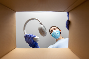 Image showing woman in mask packing headphones into parcel box