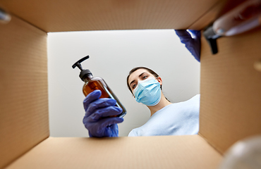 Image showing woman in mask unpacking parcel box with cosmetics