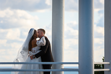 Image showing The newlyweds happily kiss in a beautiful picturesque gazebo against the sky